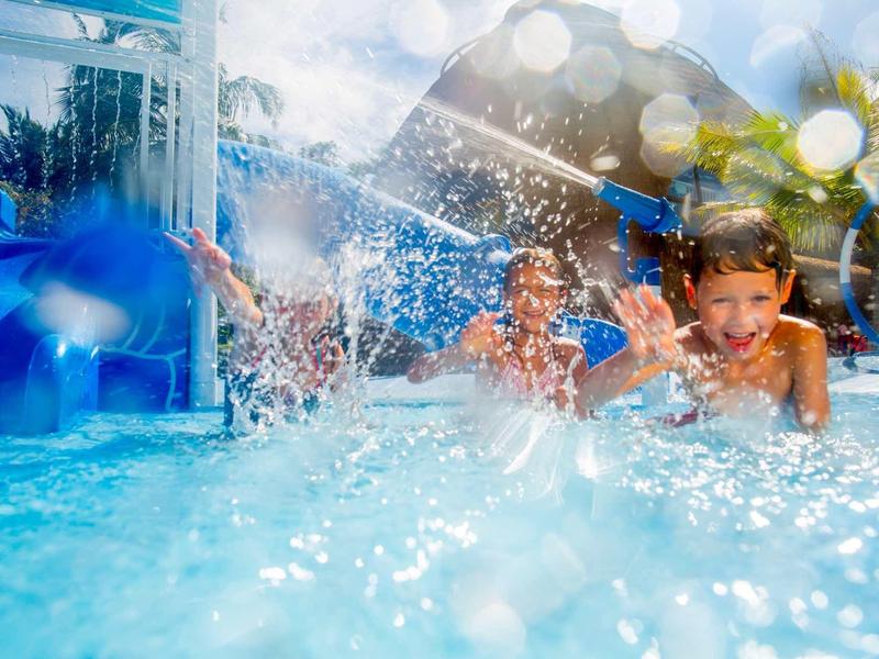 Kinder spielen fröhlich und planschen im blauen Wasser eines Schwimmbeckens an einem sonnigen Tag.