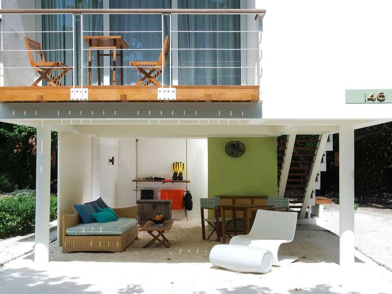 Modernes, zweistöckiges Haus mit Holzterrasse, Gartenmöbeln und weißem Liegestuhl im Außenbereich.