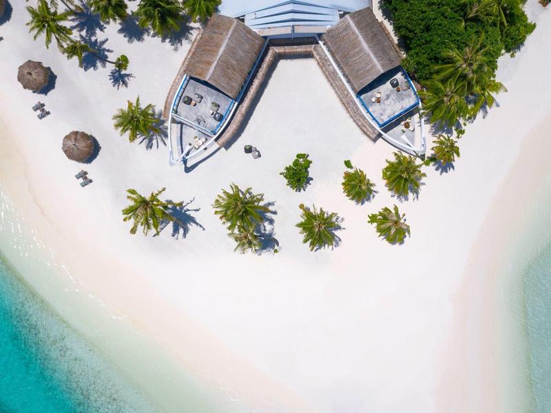 Vogelperspektive auf weiße Sandinsel mit Palmen, zwei Booten und türkisfarbenem Wasser.
