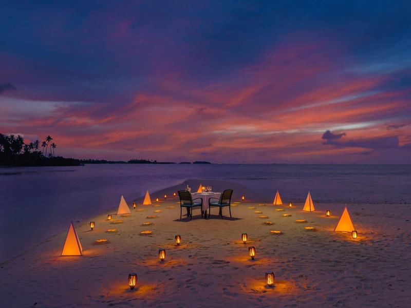 Abendstimmung am Strand mit beleuchtetem Pfad und einem gedeckten Tisch für zwei Personen.