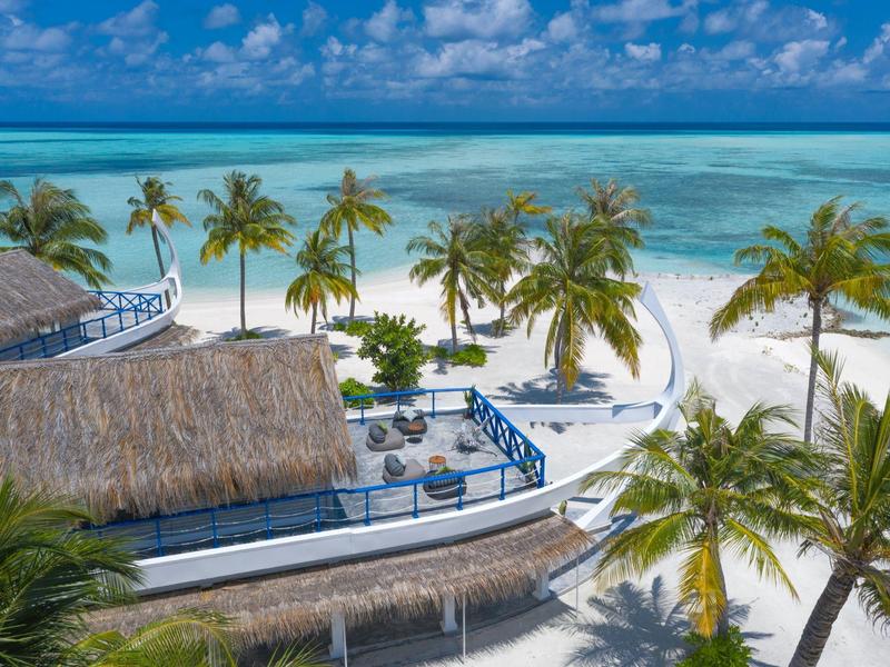 Tropischer Strand mit weißen Sand, Palmen und einem Haus mit Strohdach am türkisblauen Meer.