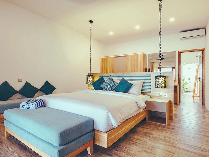 Helles Schlafzimmer mit großem Bett, blauen Kissen, Holzfußboden und gemütlicher Sofaecke.