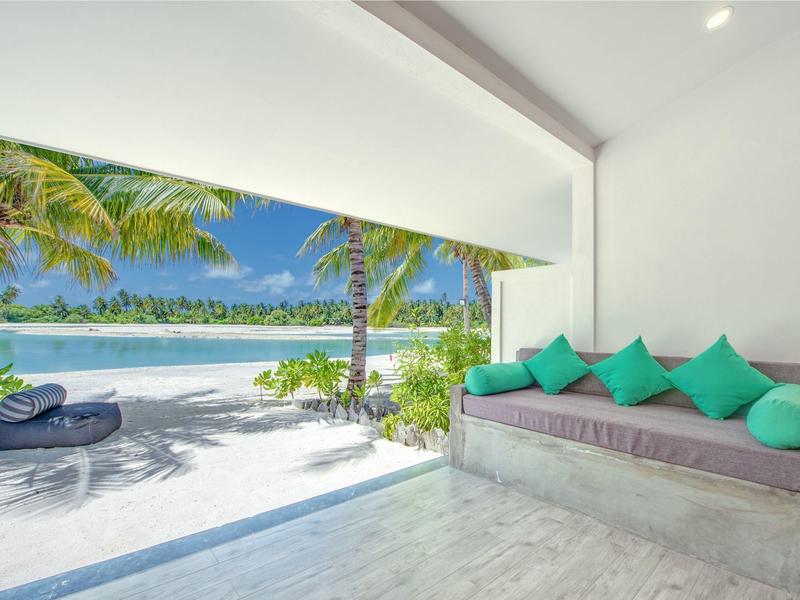 Moderner Wohnbereich mit Sofa, türkisfarbenen Kissen und Blick auf Palmen, Strand und Meer.