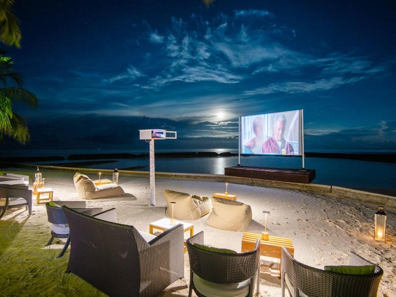 Strandkino bei Nacht mit Sitzgelegenheiten, großem Leinwand und Mondlicht über dem Meer.