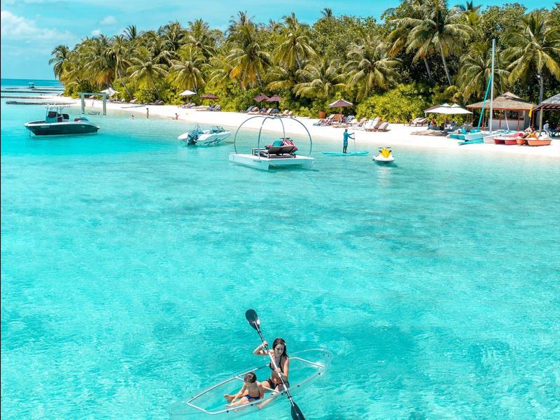 Klare türkisfarbene Lagune, Kajakfahrer, weiße Sandstrände und dichte Palmen am Ufer.