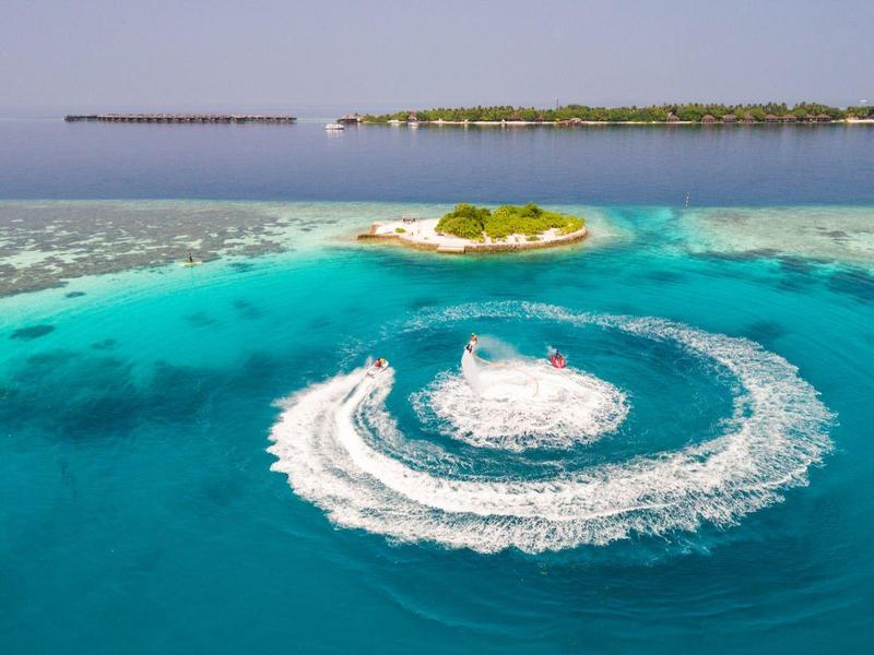 Klares türkisfarbenes Wasser mit kleinen Inseln, umkreist von einem Boot mit spiralförmiger Wellenbahn.