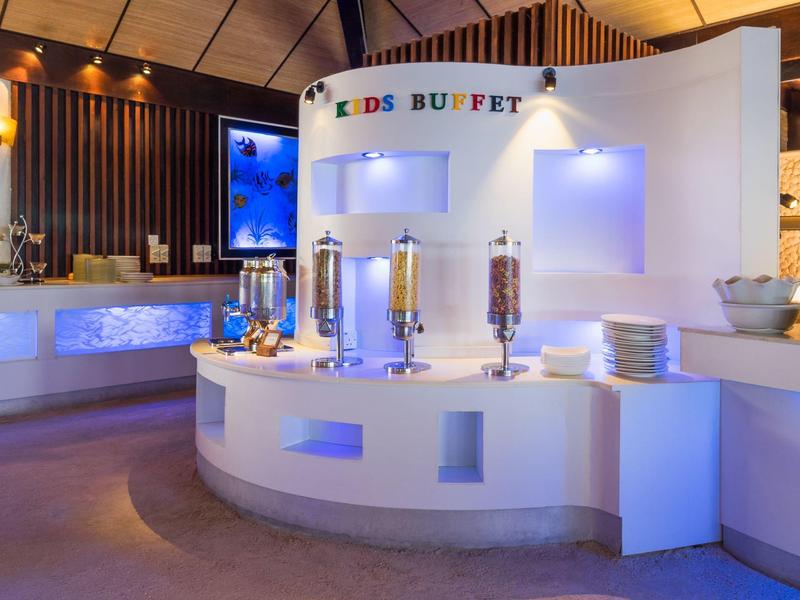 Weißes Rundbuffet mit Cerealien-Spendern und Tellern in hellem, modernem Raum.