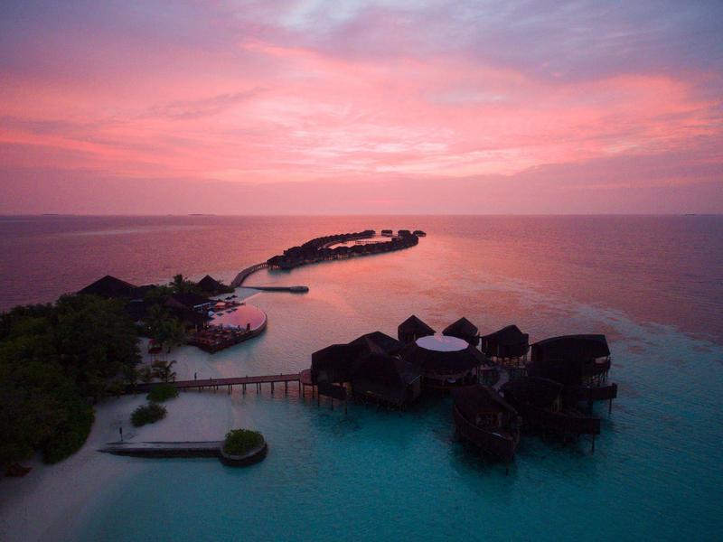 Inselresort mit Wasserbungalows in türkisblauem Meer bei rosafarbenem Sonnenuntergang.