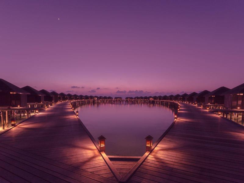 Symmetrischer Steg mit Beleuchtung und Wasserbecken bei Dämmerung in purpurnem Himmel.