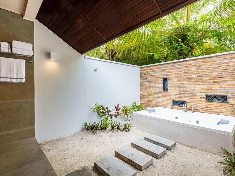Moderner Außenbereich mit Whirlpool, Steinboden, tropischen Pflanzen und Holzdachschräge.