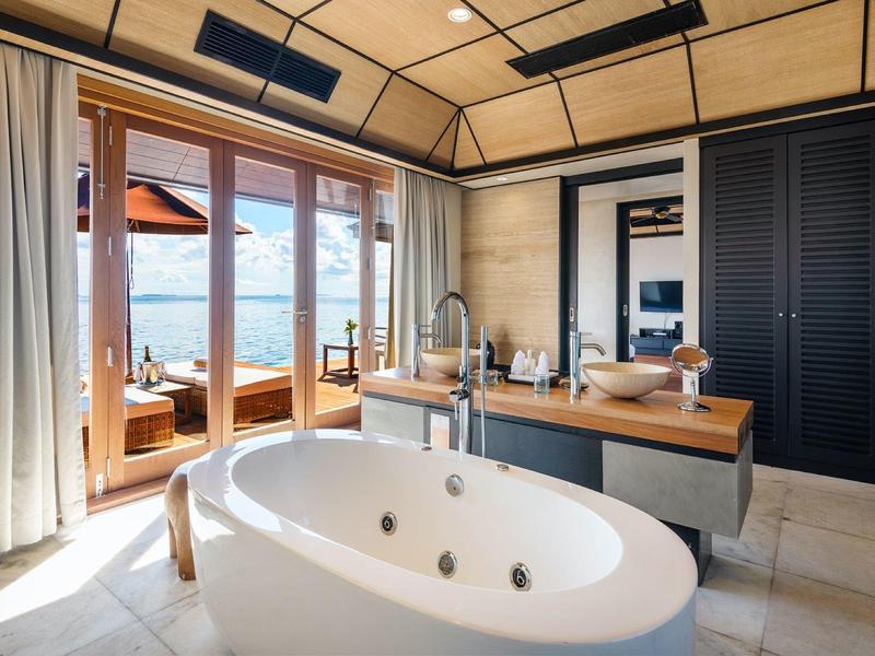 Helles Badezimmer mit freistehender Badewanne, großen Fenstern und Blick auf Terrasse und Wasser.