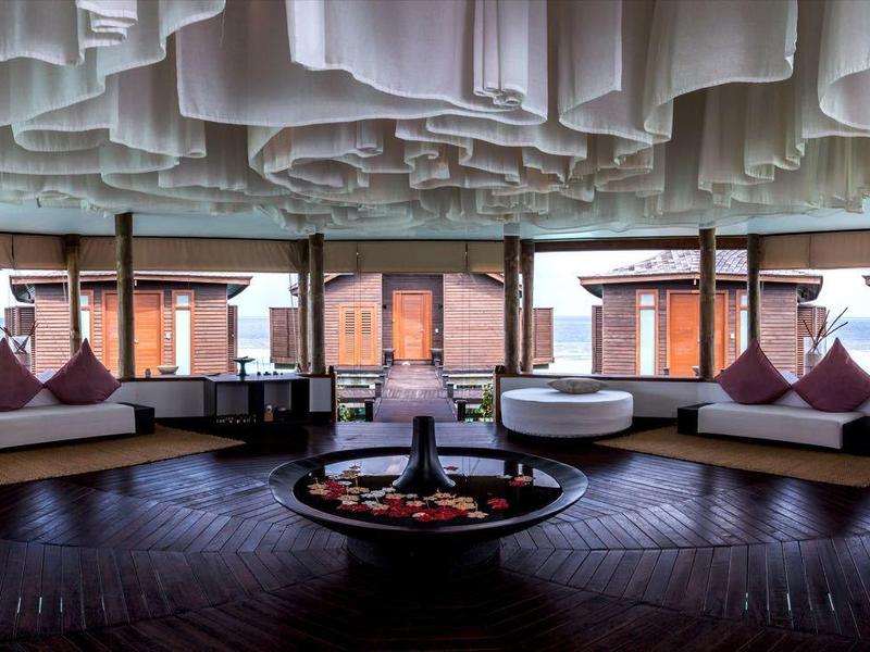 Eleganter Loungebereich mit großen Fenstern, runden Sofas, Kissen und dekorativer Decke.