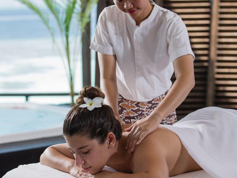 Frau erhält Rückenmassage auf weiß gedeckter Liege, entspannte Atmosphäre mit Meeresblick im Hintergrund.