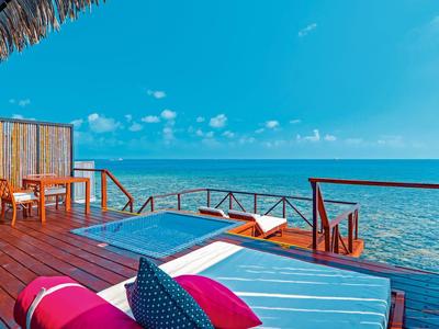 Terrazza in legno con sdraio e tavolo davanti a una laguna blu chiara sotto un cielo azzurro