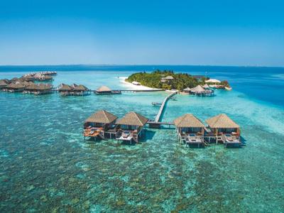 Bungalows auf Stelzen über klarem, türkisfarbenem Wasser mit kleinem Inselhintergrund und Steg.