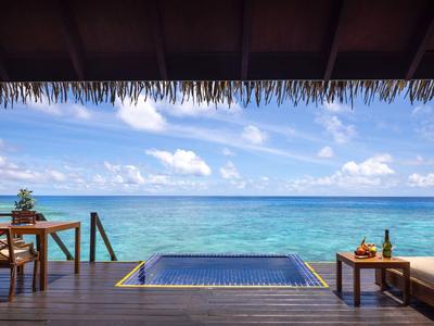 Blick auf türkisblaues Meer von Holzterrasse mit kleinem Pool und einfachen Holzmöbeln.