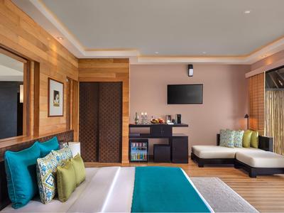 Modernes Schlafzimmer mit Holzvertäfelung, großem Bett, Sofa, Fernseher und Farbakzenten in Blau und Grün.