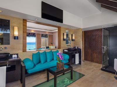 Gemütliches Zimmer mit türkisfarbenem Sofa, Glas-Couchtisch, Holzwänden und Meerblick.