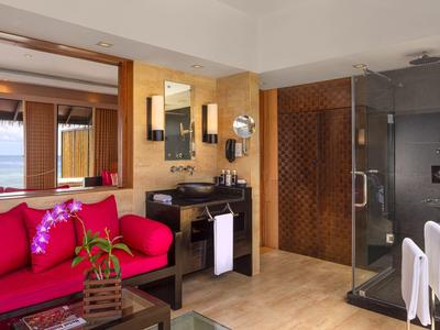 Helles Zimmer mit rotem Sofa, Holzmöbeln und moderner Glasdusche mit weißen Handtüchern.