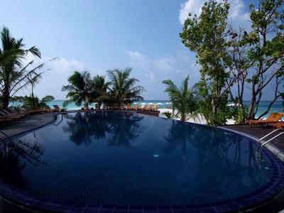 Runder Pool mit Blick auf Palmen und Strand unter blauem Himmel.