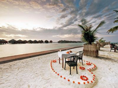 Romantisches Essensarrangement mit Herz aus Blumen auf Sandstrand am Wasser.