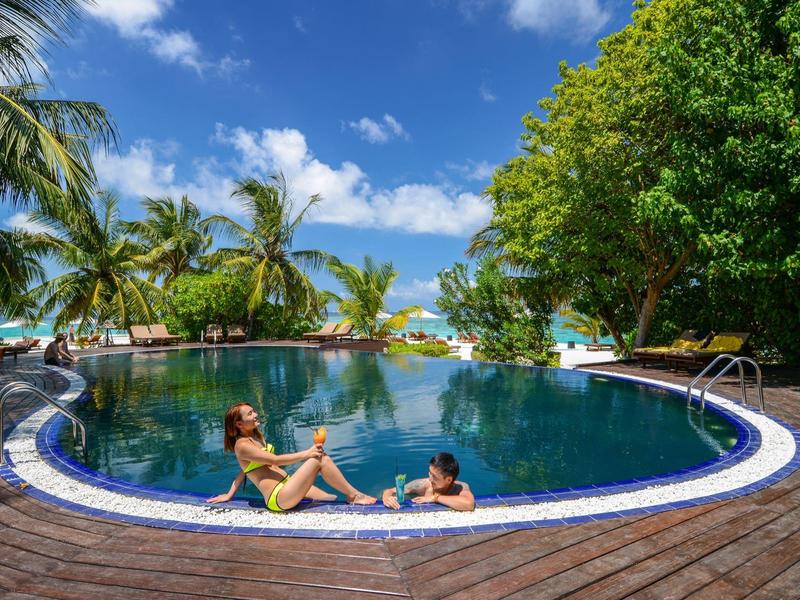 Runder Pool mit zwei Frauen, umgeben von Palmen und blauem Himmel an einem sonnigen Tag.