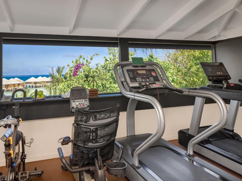 Fitnessraum mit Laufbändern, Heimtrainer und großem Fenster mit Blick auf Garten und Pool.