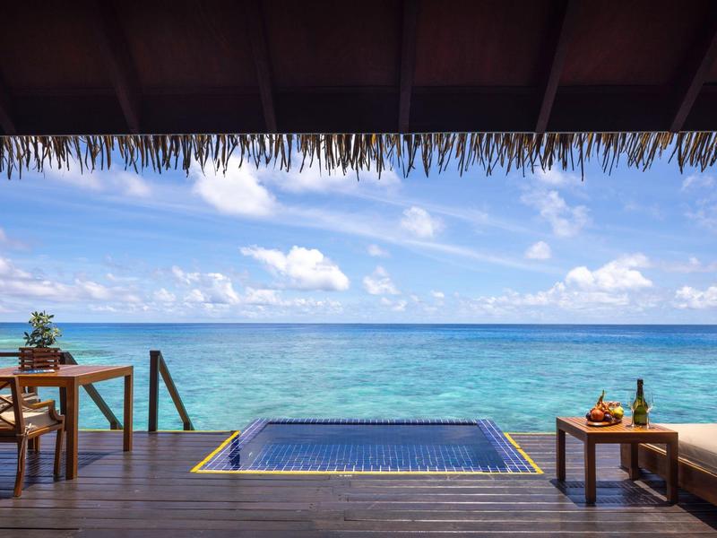Blick auf türkisblaues Meer von Holzterrasse mit kleinem Pool und einfachen Holzmöbeln.