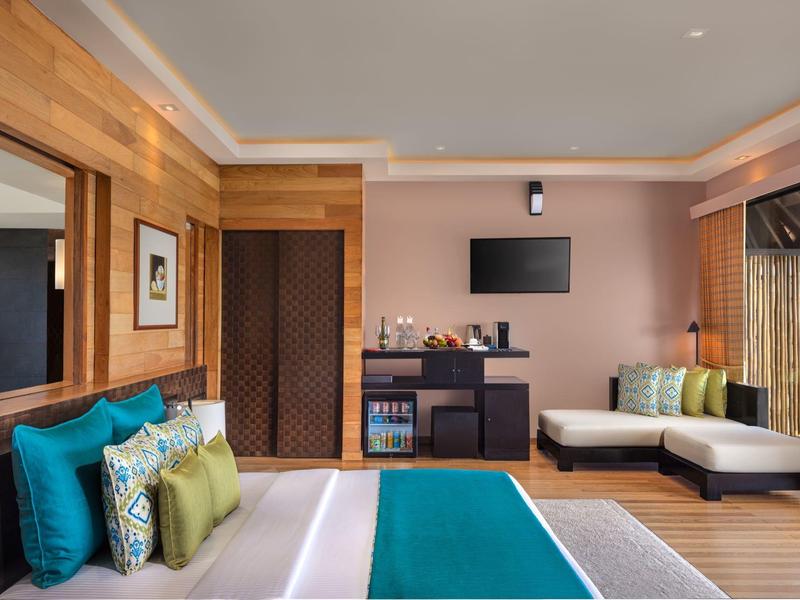 Modernes Schlafzimmer mit Holzvertäfelung, großem Bett, Sofa, Fernseher und Farbakzenten in Blau und Grün.