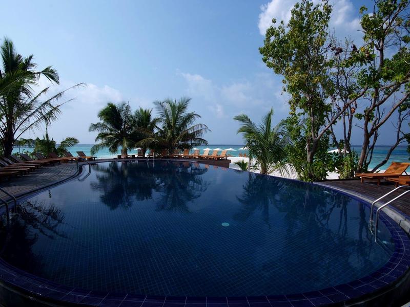 Runder Pool mit Blick auf Palmen und Strand unter blauem Himmel.