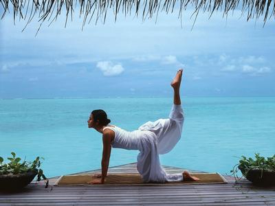 Personne pratiquant le yoga sur une terrasse avec vue sur une mer turquoise calme sous le ciel.