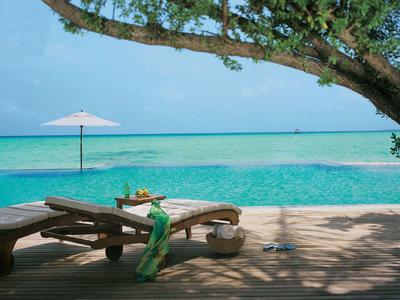 Chaises longues au bord de la piscine avec vue sur la mer turquoise sous un ciel bleu.
