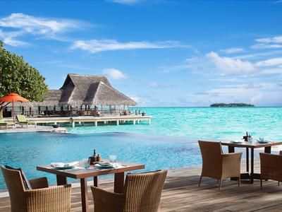 Terrasse avec tables et chaises au bord d'une eau turquoise et des bungalows