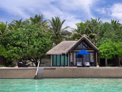 Bungalow au toit de chaume au bord de l'eau entouré d'arbres tropicaux et d'eau turquoise claire.