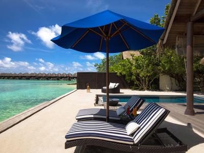 Chaise longue avec parasol bleu au bord de la piscine face à la mer et au ciel bleu.