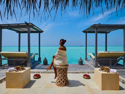 Personne assise détendue sur une terrasse avec vue sur une mer turquoise sous un ciel bleu.