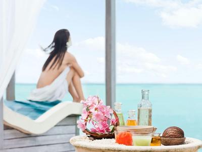 Femme en serviette assise sur chaise longue avec vue sur la mer, boissons tropicales et fruits.