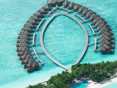 Bungalows sur pilotis de luxe en forme de croissant au-dessus de la mer turquoise avec rivage verdoyant.