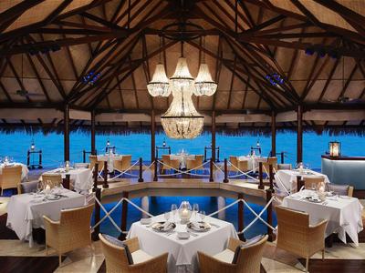 Restaurant élégant avec plafond en bois, lustres et vue sur la mer la nuit.