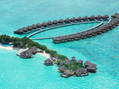 Bungalows sur l'eau sur pilotis au-dessus d'une mer turquoise claire près d'une île tropicale.
