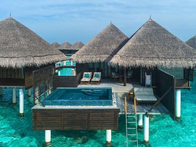 Bungalows sur l'eau avec toits en chaume et piscine privée au-dessus d'une eau turquoise.
