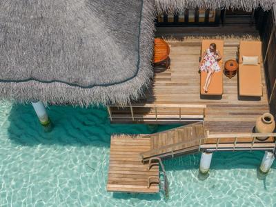 Vue d'une terrasse de bungalow sur l'eau avec des chaises longues au-dessus d'une eau turquoise claire.