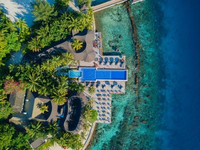 Vogelperspektive eines Resorts mit Pool, Liegestühlen und türkisfarbenem Meer