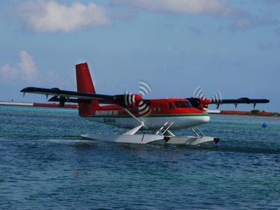 Wasserflugzeug mit roten und schwarzen Streifen startet auf einer Meeresoberfläche bei klarem Himmel.