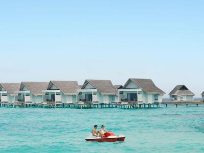 Loď s dvěma lidmi na tyrkysové vodě před bungalovy na kůlech