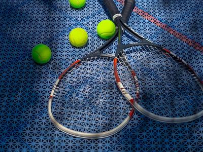 Na modrém tenisovém kurtu leží dvě tenisové rakety a čtyři žluté tenisové míčky.