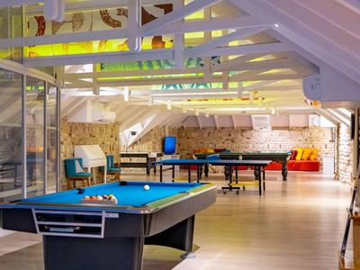 Interiér herny s kulečníkovým stolem, stolním fotbalem a sezením pod bílými dřevěnými trámy.