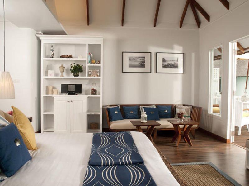 Helles Schlafzimmer mit Holzbalken, weißem Bücherregal, Holzboden und blau-weißem Bettbezug.