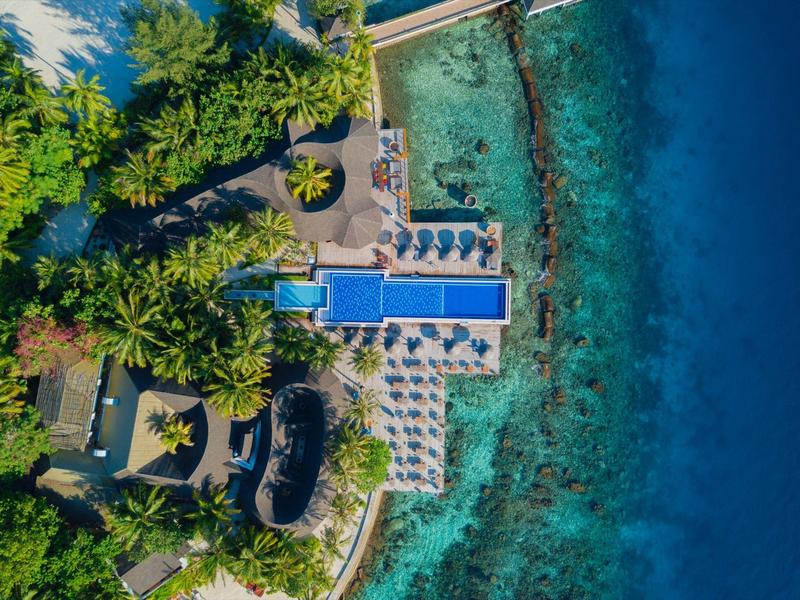 Vogelperspektive eines Resorts mit Pool, Liegestühlen und türkisfarbenem Meer