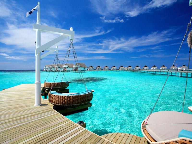 Überwasserbungalows mit einem Holzsteg, der in klares türkisfarbenes Wasser ragt unter blauem Himmel.
